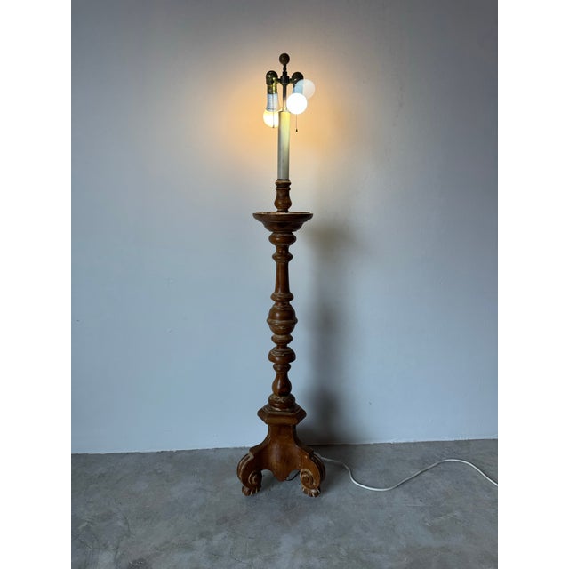 A stately 1960s Hollywood Regency floor lamp featuring an ornately turned solid wood base with elegant scrollwork feet and...