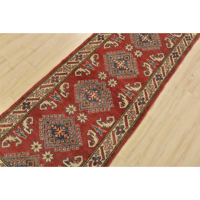 A tribal Caucasian Kazak runner hand-knotted with fine wool on a cotton foundation. This rug features geometric medallions...