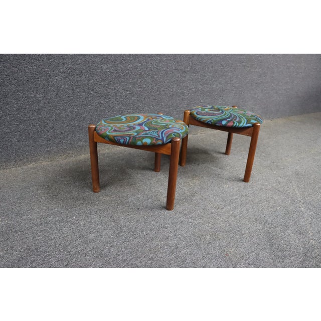 Pair of mid-century Jack Larsen style tripod footstools featuring colorful paisley upholstery and simple wooden legs....