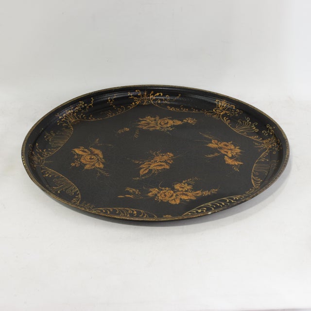 This elegant vintage round tole tray features a deep black lacquer finish serving as a dramatic backdrop for its...