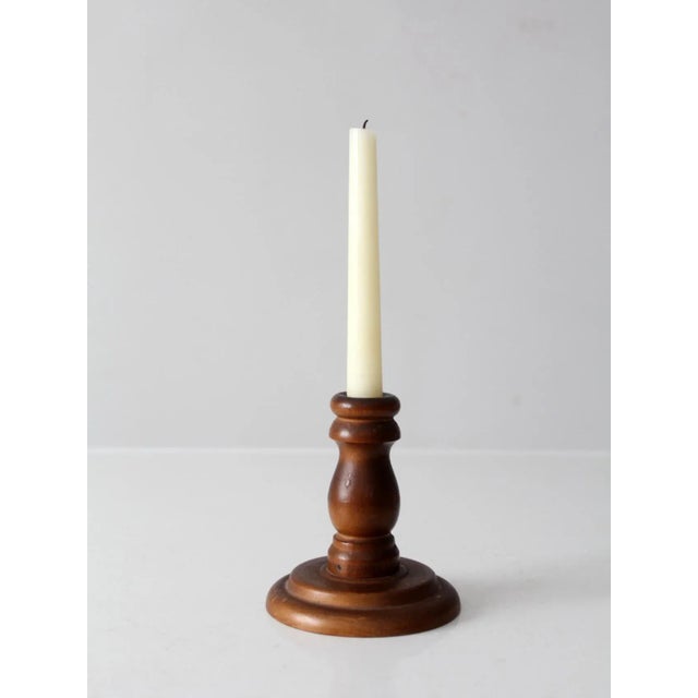 This vintage wooden candlestick holder showcases a classic turned form with a rounded base and smooth finish. The natural...
