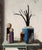 This artwork depicts a stylized family of abstract figures gathered around a collection of geometric structures, including...