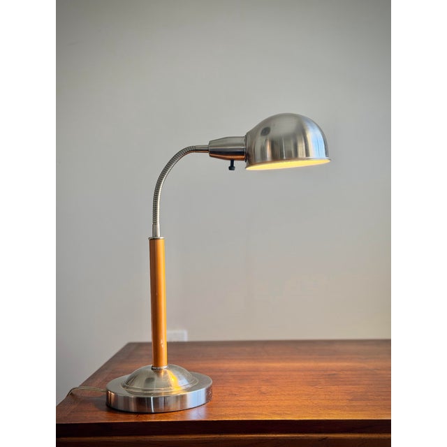 A striking vintage 1970s adjustable desk lamp combining warm orange color with cool brushed chrome for a quintessentially...