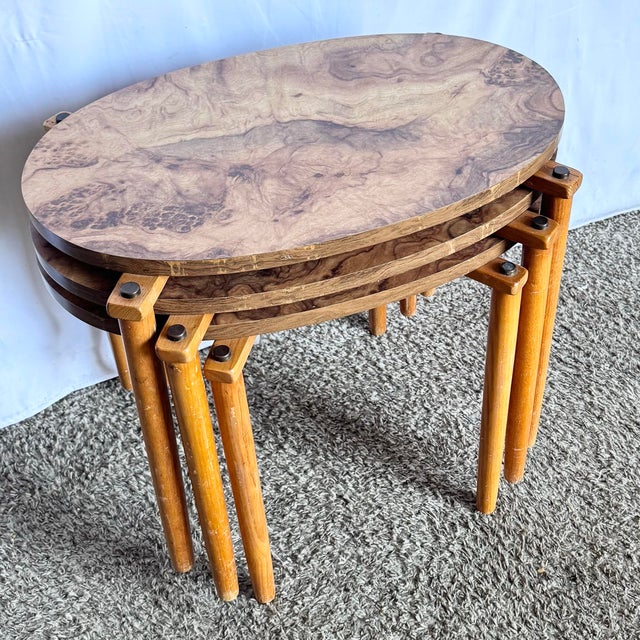 Elevate your space with this chic set of Mid Century Modern oval nesting tables, featuring warm burlwood-style laminate...