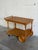 A mobile two-tier design features turned spindles, scalloped aprons, and large wooden rear wheels. An integrated push...
