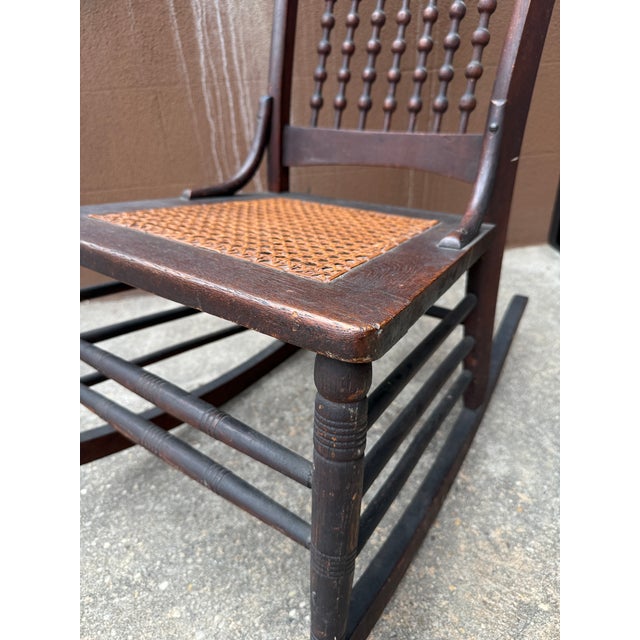 Antique rocking chair dating to the late 19th to early 20th century. Constructed in wood, likely oak, with turned legs and...
