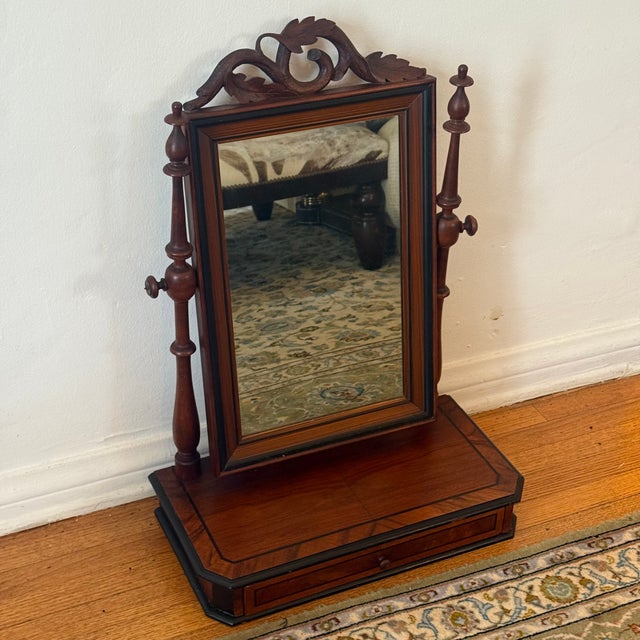 A beautifully detailed vintage tabletop vanity mirror in a rich mahogany finish, featuring turned side supports, a carved...