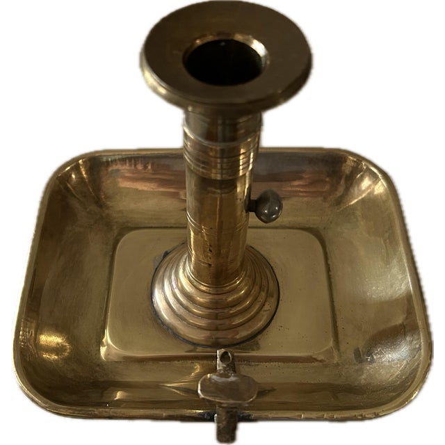 Elegant antique chamberstick in solid brass with a traditional rectangular base. The stem features a pewder shuttle to...
