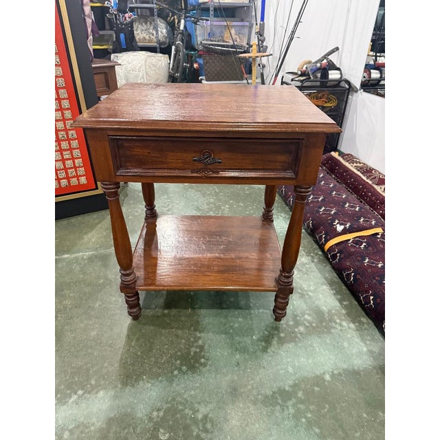 Charming vintage wooden side table featuring classic turned legs, a single dovetail-style drawer with decorative metal...