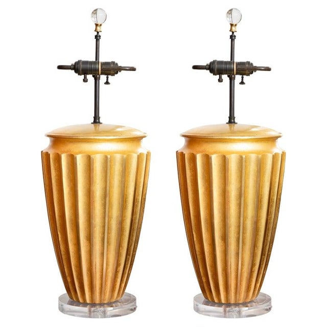 This is a striking pair of Art Deco-style gilt table lamps, featuring boldly fluted urn-form bodies with a warm hand-...