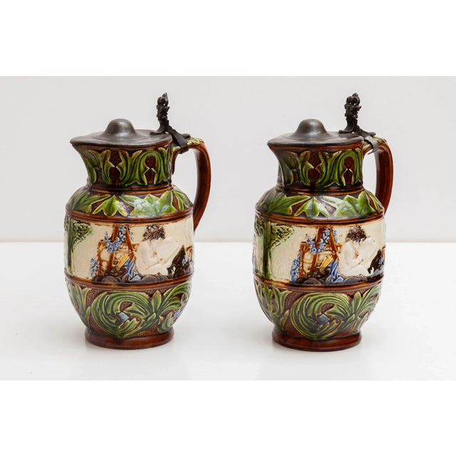 A set of 1851-1898 Belgium majolica pitchers, pottery jugs with pewter top.White hand painted cherubs sitting in a...
