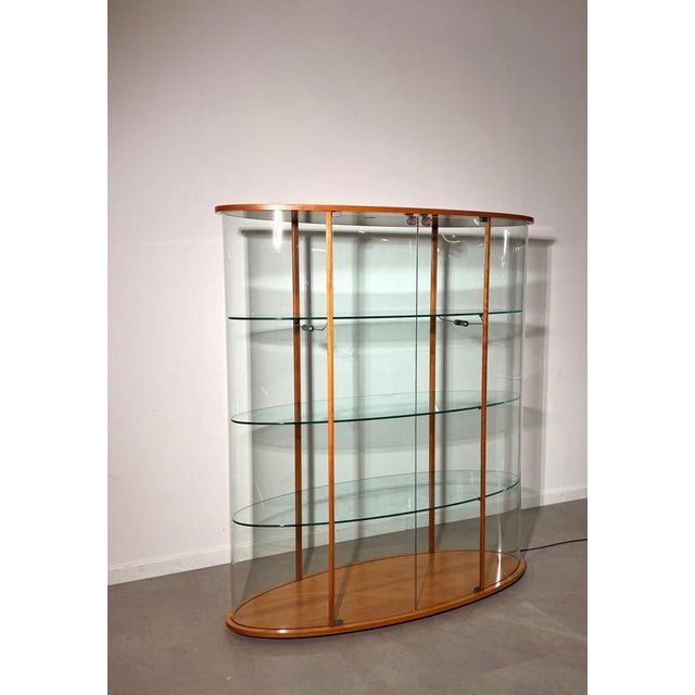 Elegant vintage display cabinet by Fiam, Italy, combining curved glass with a warm wooden frame. The oval form and slim...