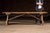 Long, low pine work bench constructed from thick, well-worn planks with a simple trestle base and pegged joinery. The top...