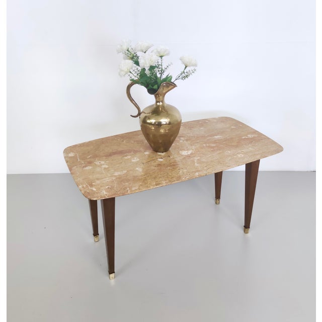 Made in Italy, 1950s. This coffee table features a beech frame with brass feet caps and a pink travertine top. Its design...