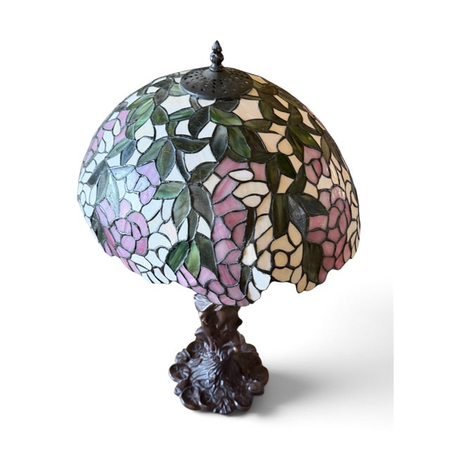 A striking Tiffany-style table lamp featuring an elaborate stained floral shade supported by a beautifully sculpted female...