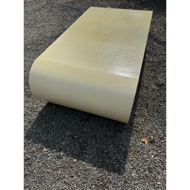 A large rectangular coffee table having a scroll base in the style of Karl Springer. The table is painted in an ivory...