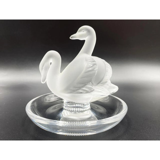 A "Deux Cygnes" ring plate by Lalique features a stunning pair of swans sculpted in frosted crystal. Swans, known as a...