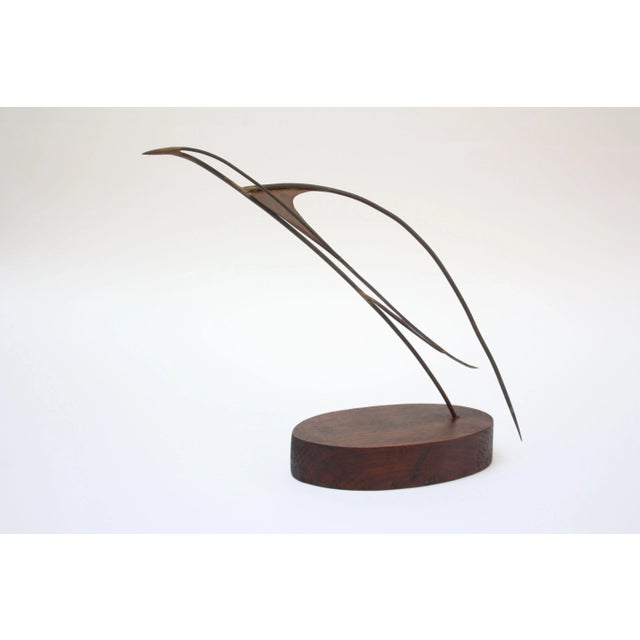 Graceful bird on base sculpture composed of soldered metal brass rods with inset copper details mounted to an oval, walnut...