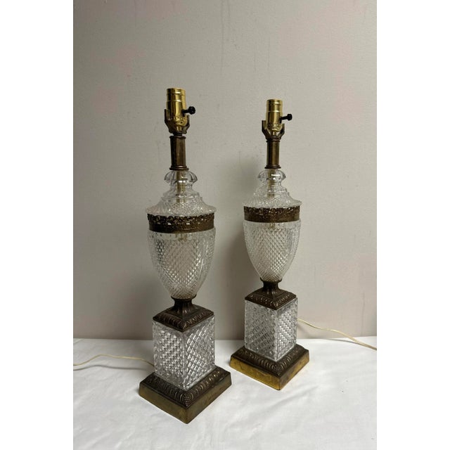 A pair of Hollywood Regency Urn form lamps with brass tone filigree accents and ornate bases. 4” W x 4”W x 29” H to the...