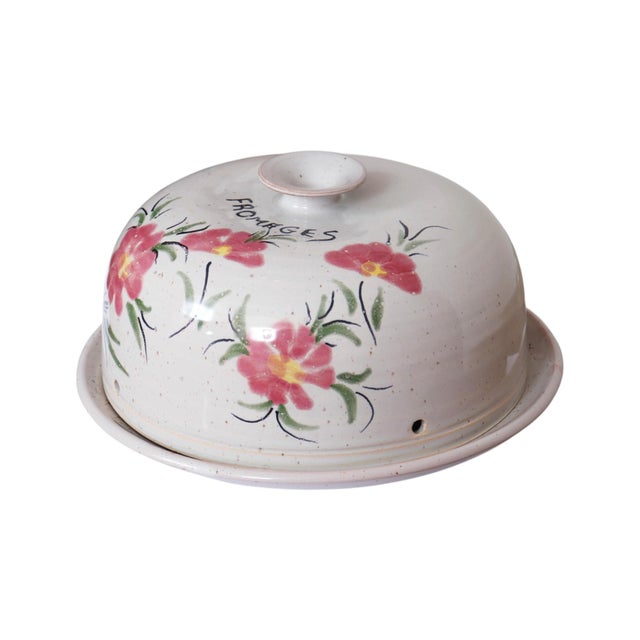 A French stoneware cheese plate with a domed lid. Hand-painted pink and yellow flowers with green leaves are set against a...