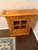 This piece is crafted from tiger maple wood and features a single door with a glass-front display.