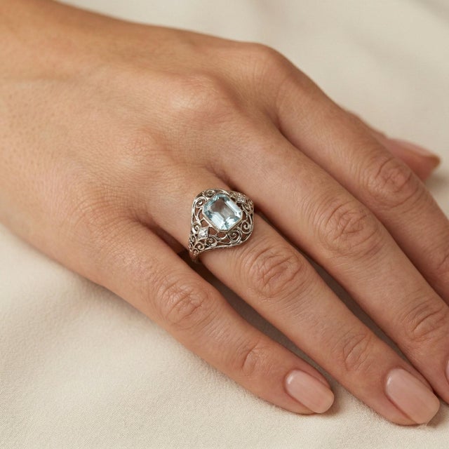 Elegant antique ring crafted in 18K white gold, featuring a faceted aquamarine center framed by intricate openwork...