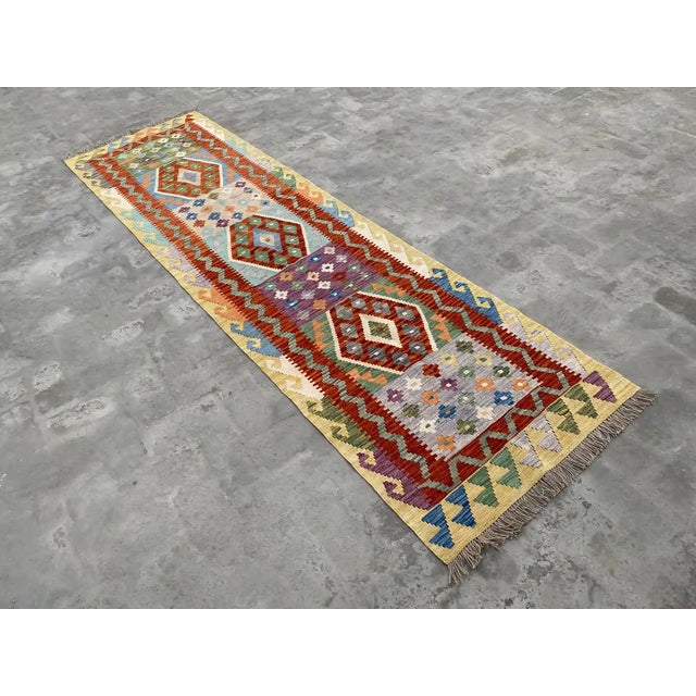 This vibrant hand-woven Kilim runner rug showcases a beautiful array of geometric patterns in an eye-catching color...