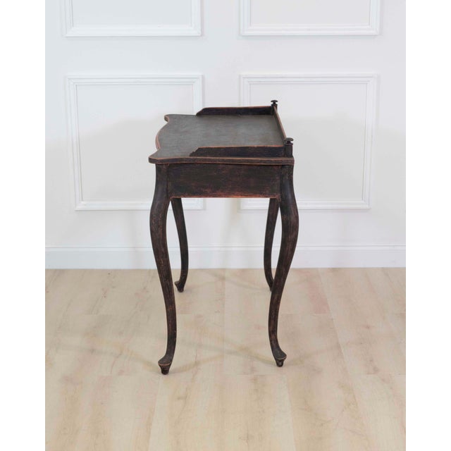 Made in Sweden in the twentieth century, this black Rococo-style writing desk has a tabletop framed on three sides and a...