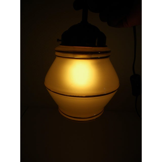 Pendant light approximately 28 cm high. Short brass stem, metal base. The shade is a closed opaline glass, surrounded by...