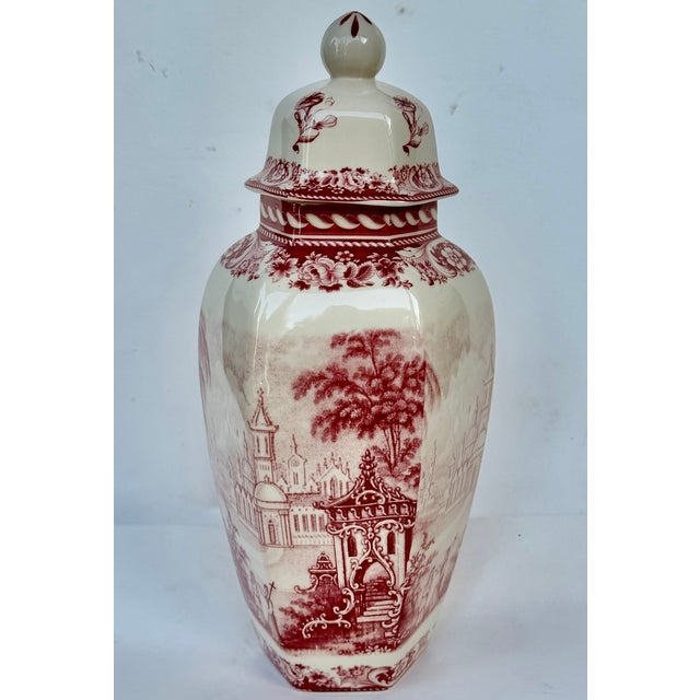 A tall English porcelain lidded jar decorated in red and white with chinoiserie scenes of pagodas, trees and gardens....