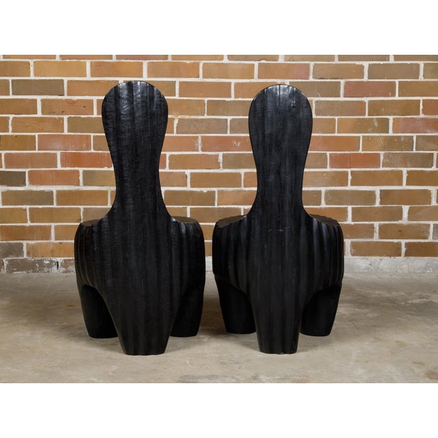 A sculptural pair of Midcentury African wood spoon back black chairs with carved reeded bases. This sculptural pair of...