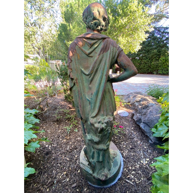 Cast iron statue of a farmer holding a scythe, and standing next to a sheaf of wheat. Classical Roman style, with a face...