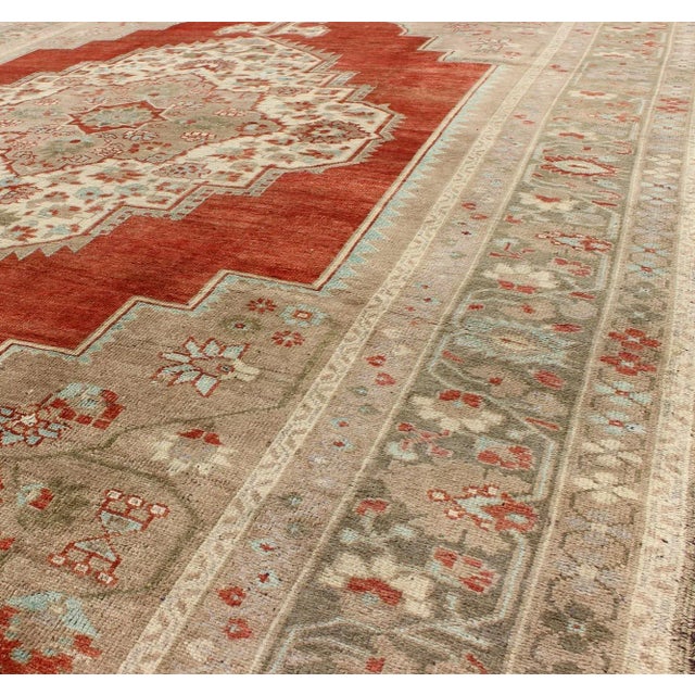 This beautiful classic vintage Oushak has a large medallion in rust/orange red complemented by light green border and warm...