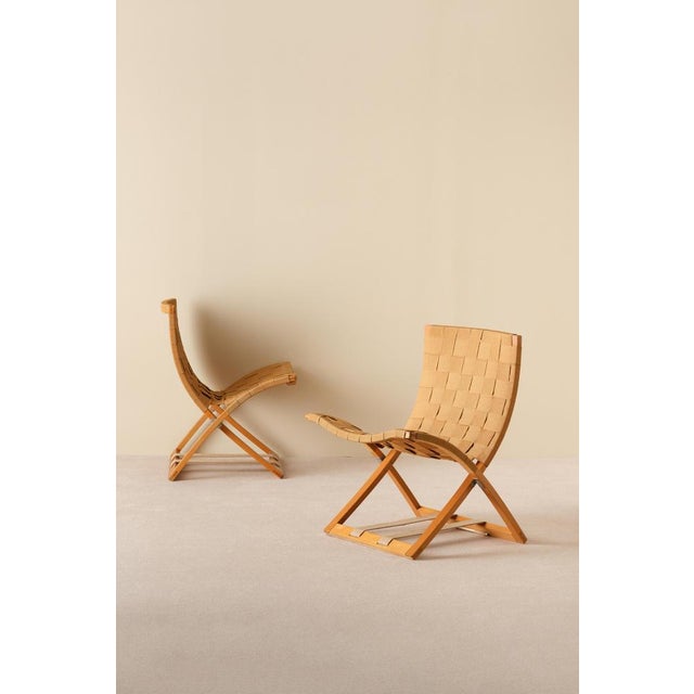 A beautiful pair of foldable lounge chairs in warm-toned wood with woven seats and backs. The curved, ergonomic shape...