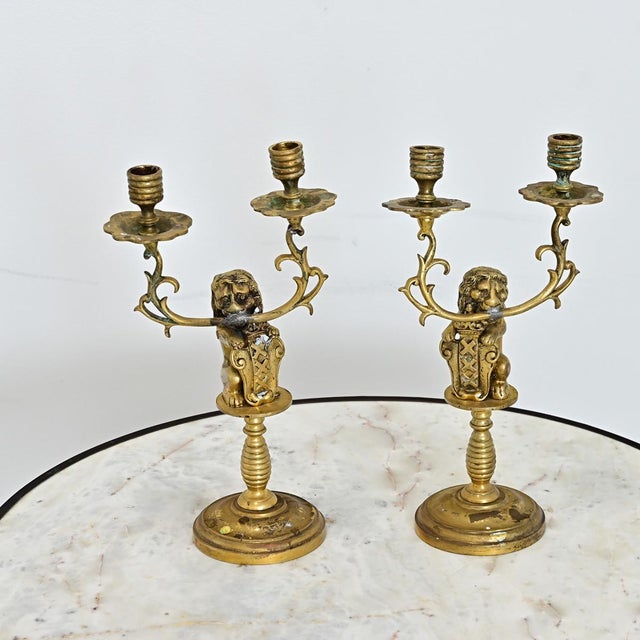 A Dutch pair of 19th century brass candelabra featuring heraldic lions of the Amsterdam coat of arms who clutch the...