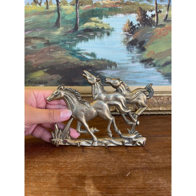 Charming vintage brass toned wall hook rack featuring a trio of galloping horses in mid-stride. The sculptural relief...