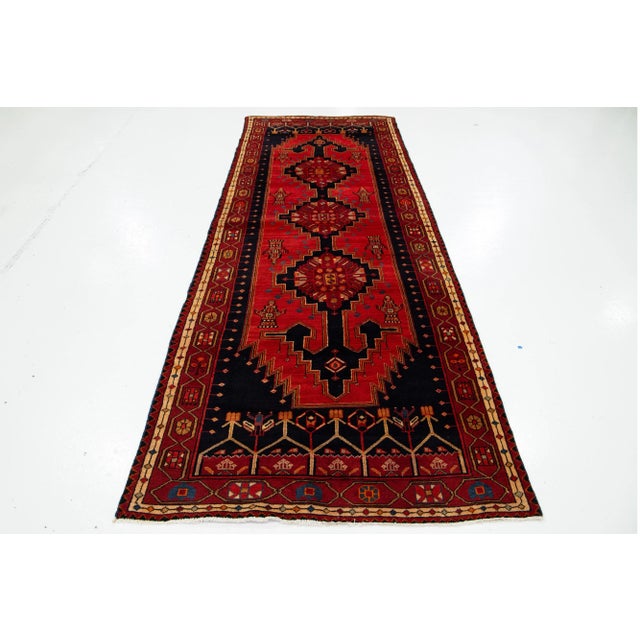 This vintage handmade Persian wool rug has a red field and navy blue and orange accents throughout the tribal pattern....