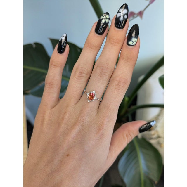 A rare padparadscha sapphire glows in its signature blend of pink and orange, framed by a halo of sixteen earth-mined...