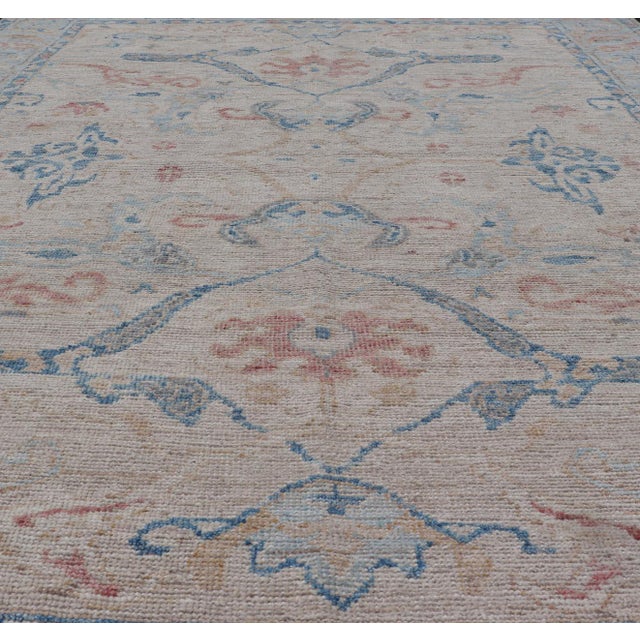 Hand knotted Oushak made in wool with a field is backed by a ivory color, with a light blue border, etched with elegant...