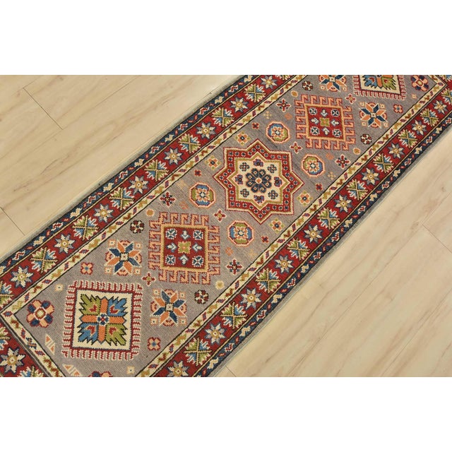 A tribal Caucasian Kazak runner hand-knotted with fine wool on a cotton foundation. This rug features geometric medallions...