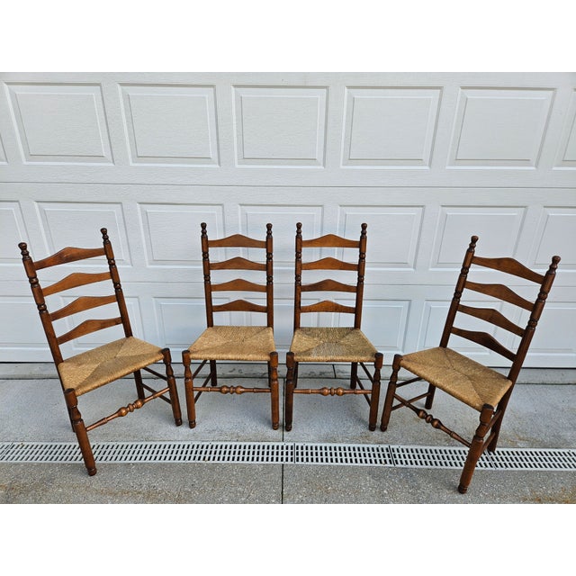 A set of four vintage wooden ladder-back side or dining chairs featuring woven rush seats and turned legs with a centered...