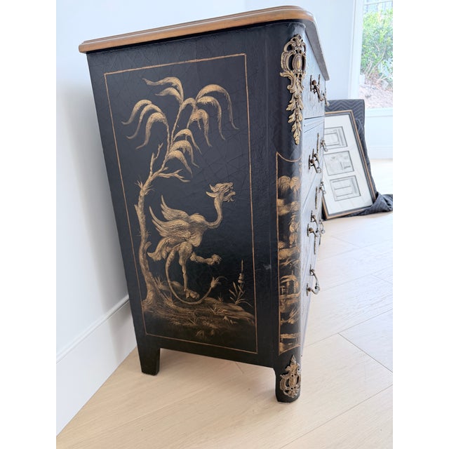A black lacquer Chinoiserie bombe chest featuring hand-painted gilt Asian landscape scenes, ornate antique brass hardware,...