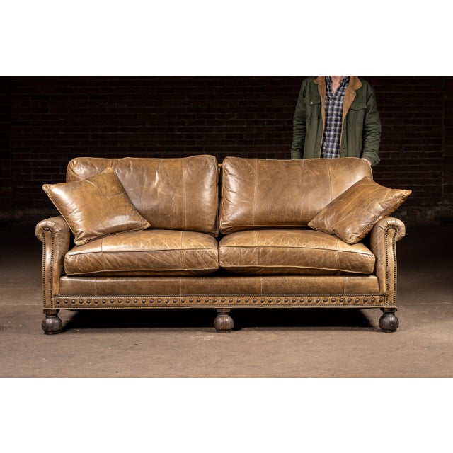 Three-seat sofa upholstered in warm, distressed brown leather with a naturally worn, crackled surface that highlights the...