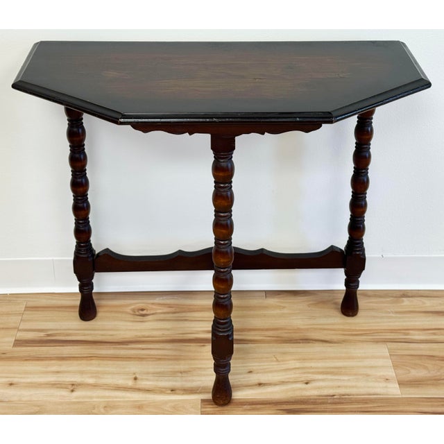 Vintage carved wood demilune table featuring angular beveled top and three bobbin legs attached by carved stretchers....