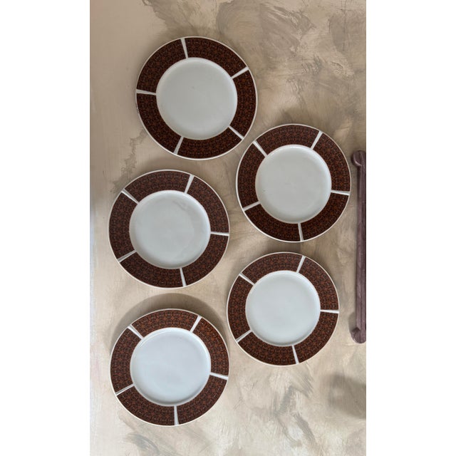A handsome set of five vintage ceramic dinner plates featuring a bold brown scrollwork border with an iron-gate–style...