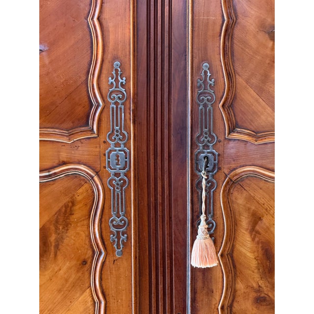 An 18th century Louis XV fruitwood armoire with a shaped cornice above a pair of paneled doors, each door fitted with...