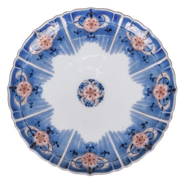 A set of 13 matching Japanese Imari porcelain plates with a scalloped, radially-paneled rim, painted in underglaze blue...