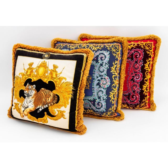 Collection of Three Atelier Versace Throw Pillows, comprising: pair in red and blue paisley pattern and one with recumbent...