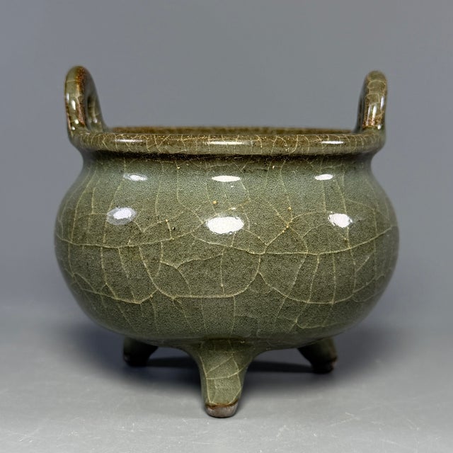 Classic Chinese official‑style celadon porcelain tripod incense burner. It features upright double handles, rounded...