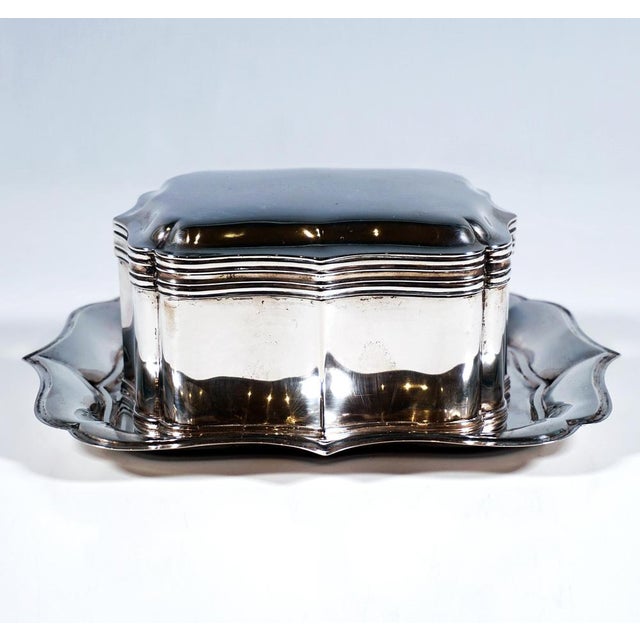 Silver lidded tin on a matching display tray; both items of a curved, elegantly shaped design in the neo-baroque style,...